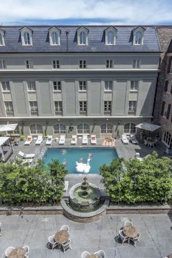 A luxury hotel courtyard with a central pool, surrounding sun loungers, shaded seating areas, and elegant stone buildings around the atrium, ending with a bright blue sky.