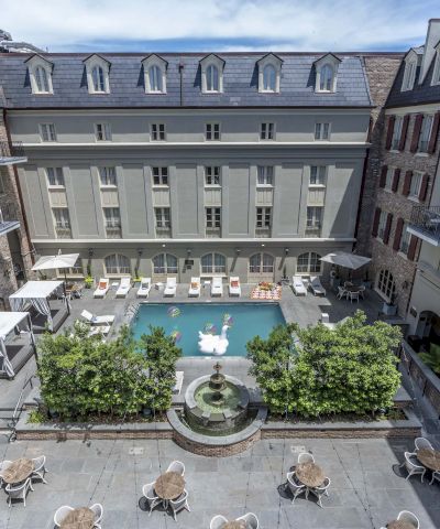A luxury hotel courtyard with a central pool, surrounding sun loungers, shaded seating areas, and elegant stone buildings around the atrium, ending with a bright blue sky.