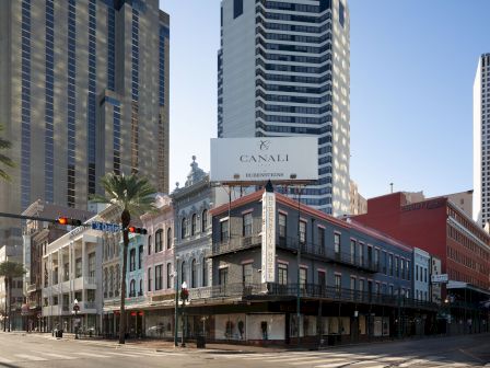 A street scene with tall modern buildings and a classic two-story storefront on a corner, under clear skies.