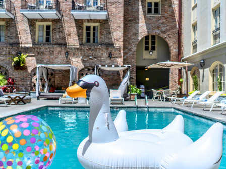 Poolside vacation vibe with floaties, inflatable swan, and colorful beach balls by a sunny hotel pool. 140 characters exactly, ending with a period.