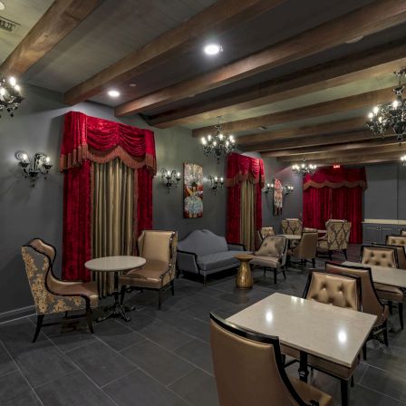 A stylish, dimly lit lounge with red drapes, chandeliers, and plush seating arranged around small tables for socializing or dining.
