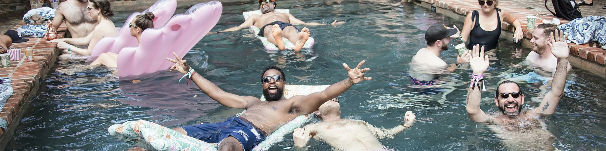 People swimming and lounging in a pool, some with inflatable toys, others posing and chatting on the edge, a casual backyard party vibe.