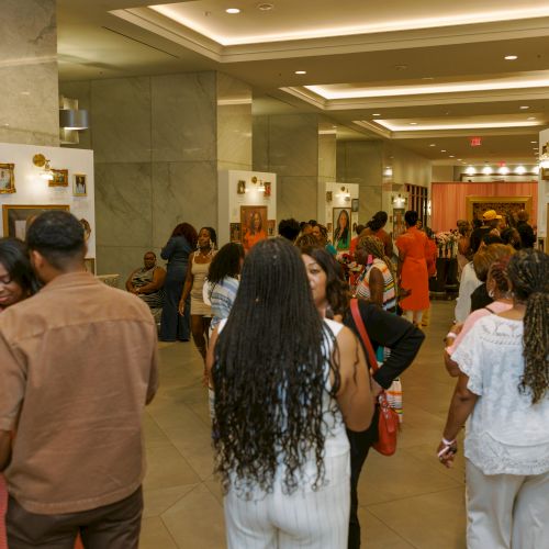 Crowd tours a museum gallery with framed portraits and exhibits in a bright marble lobby.