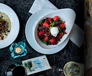 A restaurant scene with a chef in whites beside plates of burgers, fries, steak, and berry desserts.