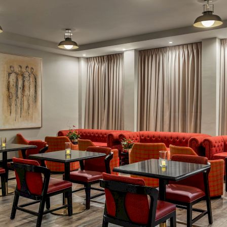 A cozy restaurant lounge with red upholstered booths, glass tables, pendant lights, and tall beige curtains.