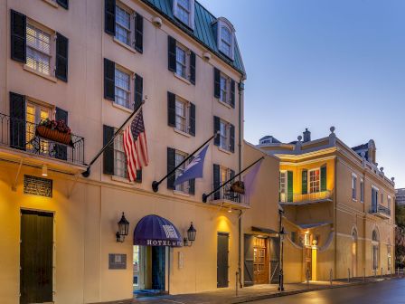 A historic hotel exterior with balcony windows, hanging flags, and warm lights at dusk.