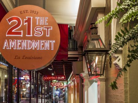 A street entrance sign reads &ldquo;21st Amendment&rdquo; with &ldquo;La Louisiane&rdquo; on a circular marquee outside an alley bar.