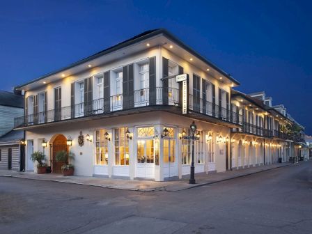 A warmly lit hotel building with balconies and signage at night, set along a quiet street under a deep blue sky.